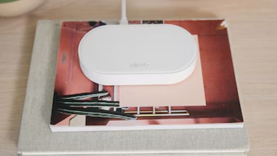  Somfy Connectivity Kit device placed on a table, showing a sleek and compact white design, connected with a USB power cable. Ideal for managing smart home automation systems like motorised blinds, curtains, and lighting through a central hub.